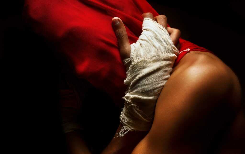 A dramatic close-up of a bandaged hand grasping red fabric, embodying tension and strength.